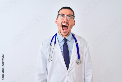 Young doctor man wearing stethoscope over isolated background angry and mad screaming frustrated and furious, shouting with anger. Rage and aggressive concept. © Krakenimages.com