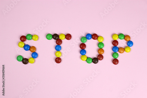 Word stop of multicolored candies on pink background
