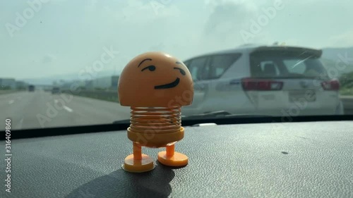 Emoji / Smiley toy on dashboard of a car travelling on highway / freeway / expressway / road
