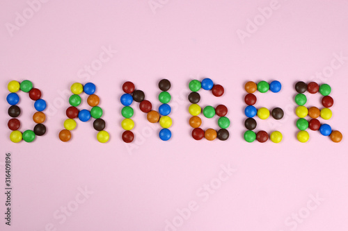 Word danger of multicolored candies on pink background