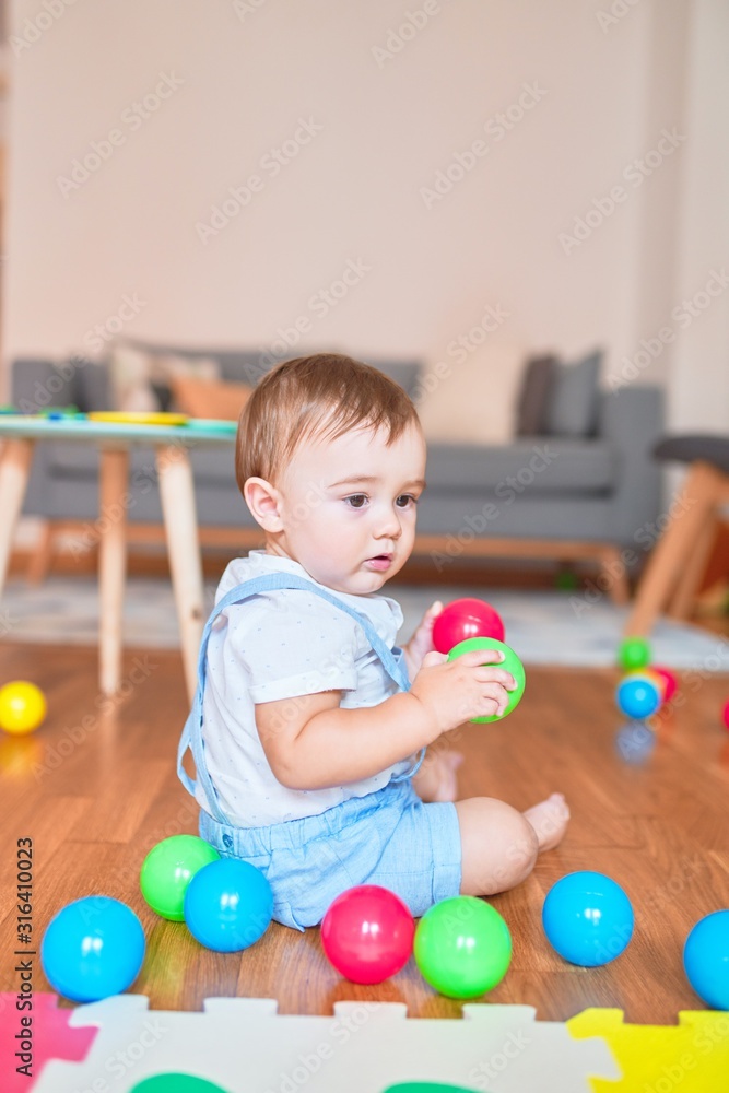 Obraz premium Beautiful toddler sitting on the floor playing with small colorful balls at kindergarten