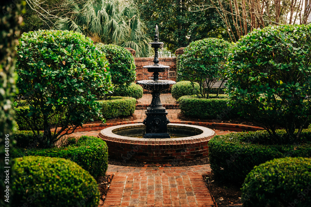 Outdoor Green secret garden with fountain in the middle and red brick and black iron gate