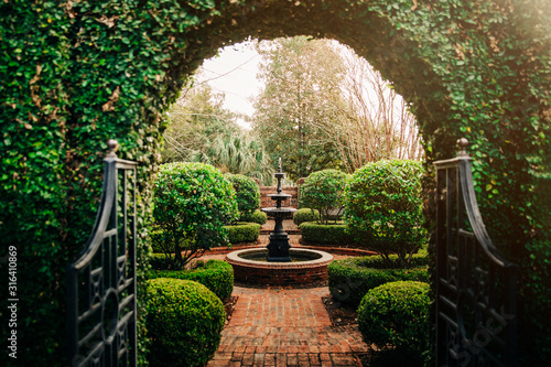 Outdoor Green secret garden with arched entry and gate and a fountain in the middle and red brick and black iron gate