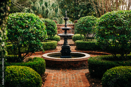 Outdoor Green secret garden with fountain in the middle and red brick and black iron gate