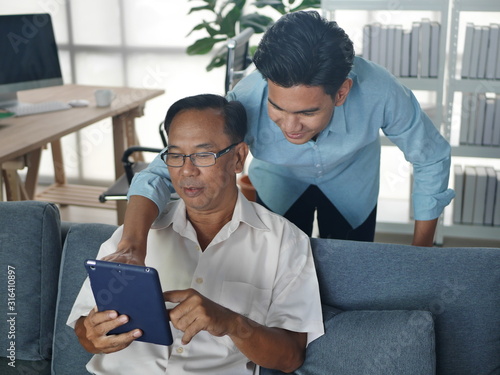 the lifestyle portrait of  the asian young man son takes care of the old father health and medication in their home and enjoy  mobile technology together 