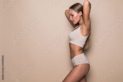 Young sexy woman with perfect body in underwear standing on beige background