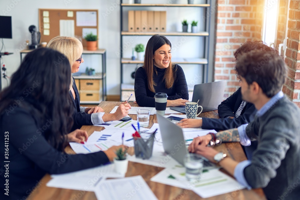 Group of business workers smiling happy and confident. Working together with smile on face using laptop and speaking at the office Group of business workers smiling happy and confident. Working together with smile on face using laptop and speaking at the office