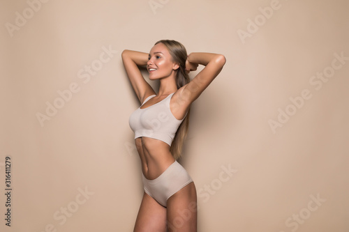 Young woman in underwear on beige background. Fitness, diet, skin and body care