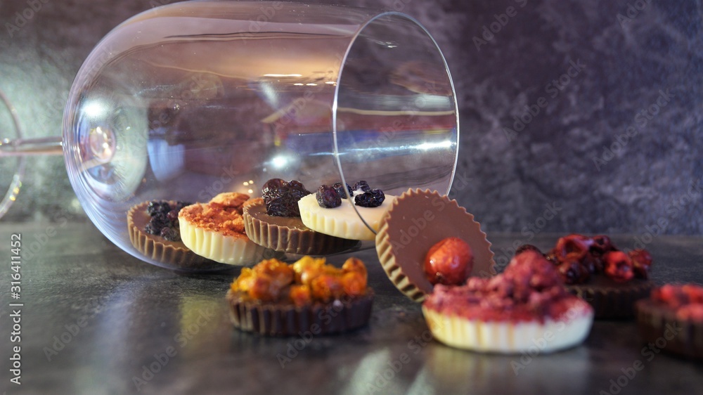 chocolate candies decorated with berries in a glass goblet on a black background chocolate candies decorated with berries in a glass goblet on a black background