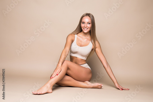 Young pretty woman sitting on the floor in underwear isolated on beige background