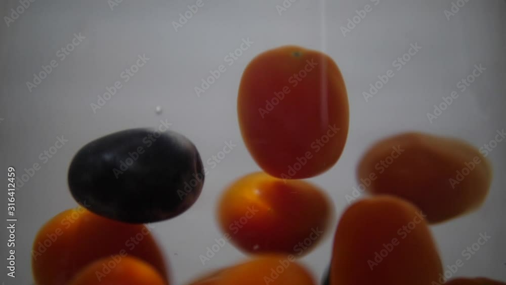 Black grapes drops into swirling red cherry tomatoes in slow motion Black grapes drops into swirling red cherry tomatoes in slow motion
