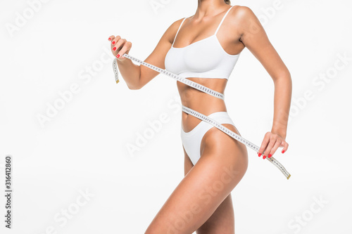 Woman measuring toned waist. Cropped image of woman in white bra and panties measuring her waist while standing isolated on white background photo