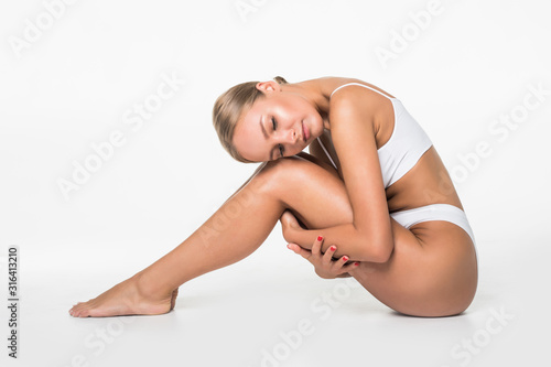 Wellness and beauty concept, beautiful slim woman in white underwear sitting on white floor isolated