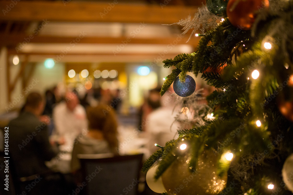 Christmas tree with decoration and people dining in the background