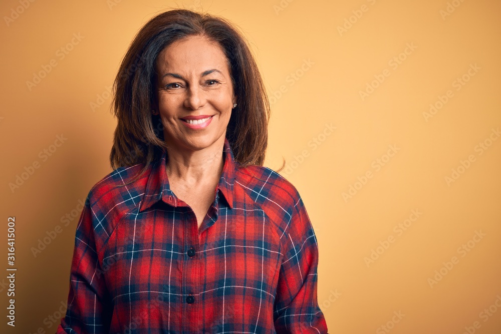 Middle age beautiful woman wearing casual shirt standing over isolated yellow background with a happy and cool smile on face. Lucky person. - obrazy, fototapety, plakaty 
