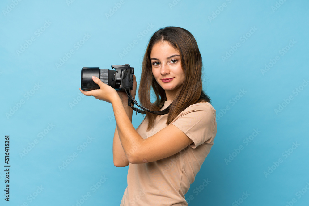 Young brunette girl over isolated blue background with a professional camera Young brunette girl over isolated blue background with a professional camera