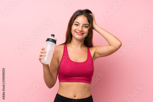 Young sport girl over isolated pink background with sports water bottle