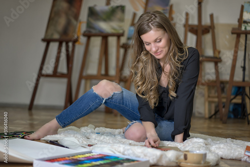 Artist woman sits on the floor and paints in art studio.