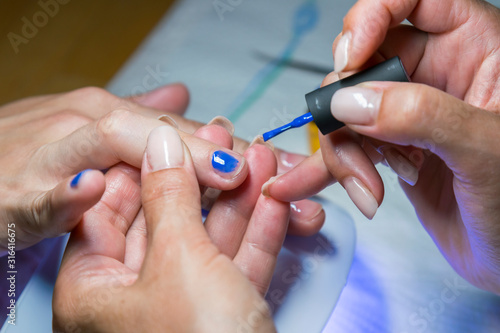 Beautiful manicure process. Nail polish being applied to hand, polish is a blue color. close up