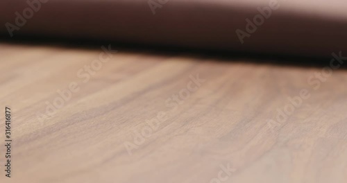 Slow motion man unroll brown leather piece on walnut table closeup