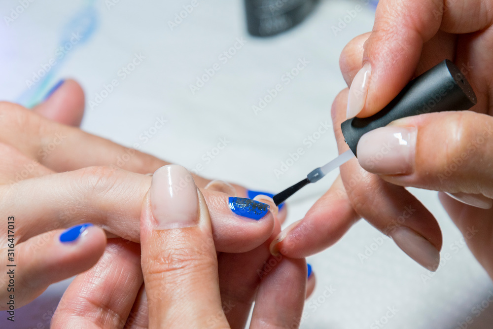 Beautiful manicure process. Nail polish being applied to hand, polish is a blue color. close up Beautiful manicure process. Nail polish being applied to hand, polish is a blue color. close up