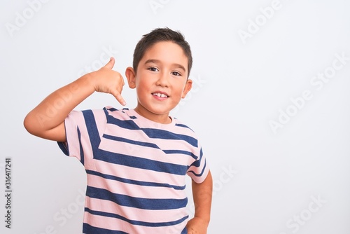 Beautiful kid boy wearing casual striped t-shirt standing over isolated white background smiling doing phone gesture with hand and fingers like talking on the telephone. Communicating concepts.