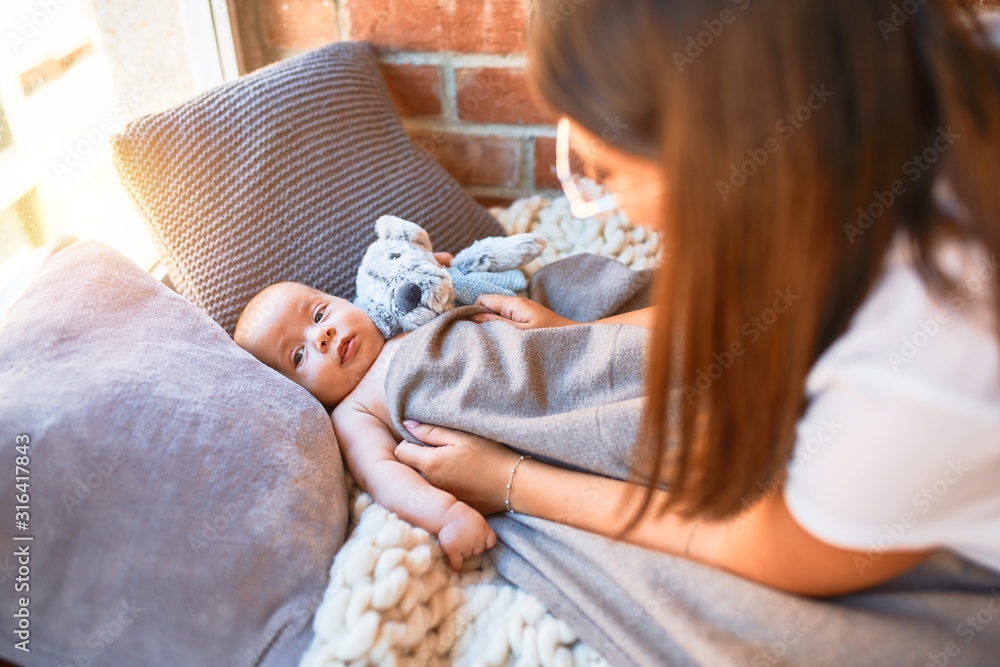Young beautifull woman and her baby on the floor over blanket at home. Newborn and mother relaxing and resting comfortable with doll - obrazy, fototapety, plakaty 