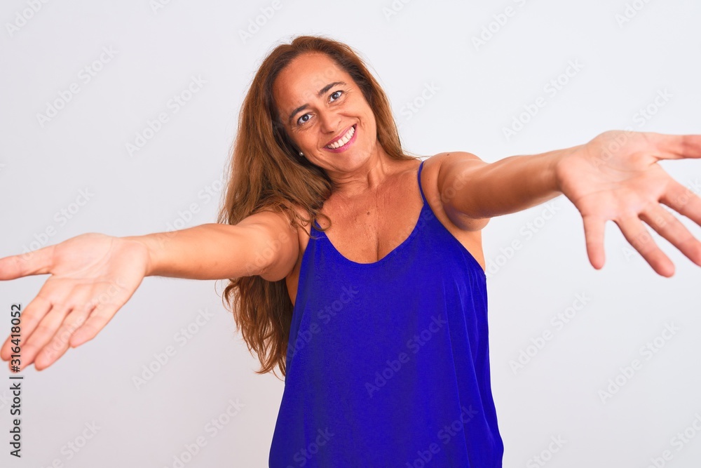 Middle age mature woman standing over white isolated background looking at the camera smiling with open arms for hug. Cheerful expression embracing happiness.
