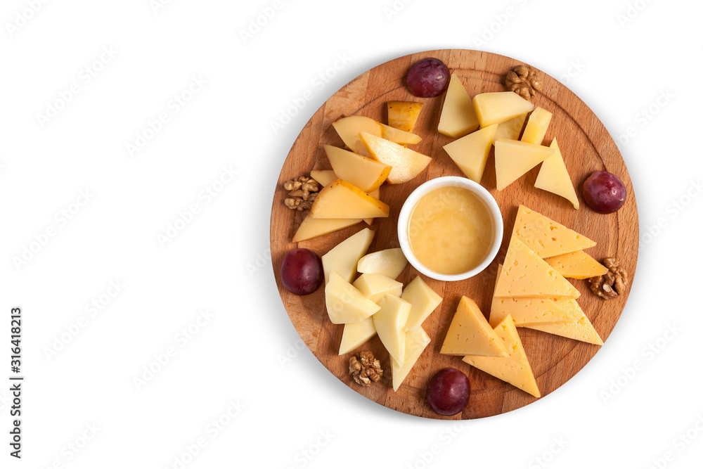 Fototapeta premium Cheese platter on a round wooden plate with walnuts, honey and grapes. Isolated, horizontal orientation, top view, copy space