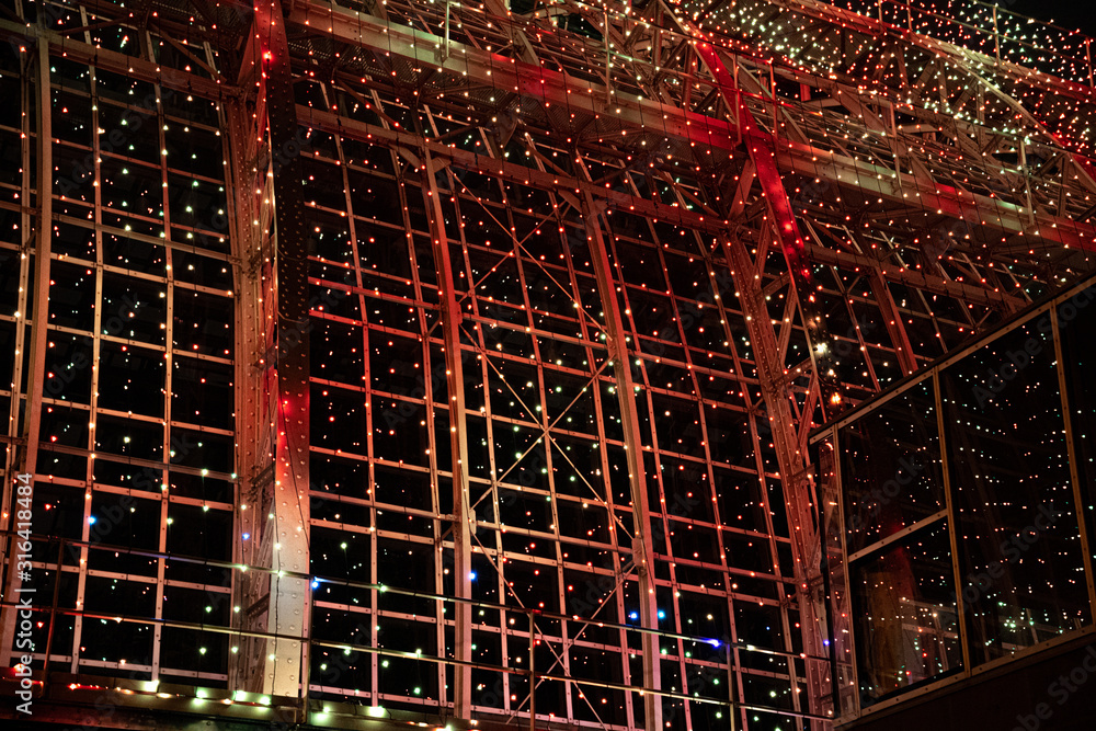 Metal grid construction lighted with shiny illuminations. Urban textures of modern architecture. Abstract background of Christmas lights in night. New Year celebration backdrop with copy space.