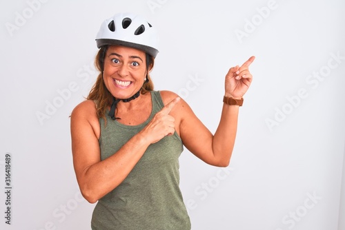 Middle age mature cyclist woman wearing safety helmet over isolated background smiling and looking at the camera pointing with two hands and fingers to the side.