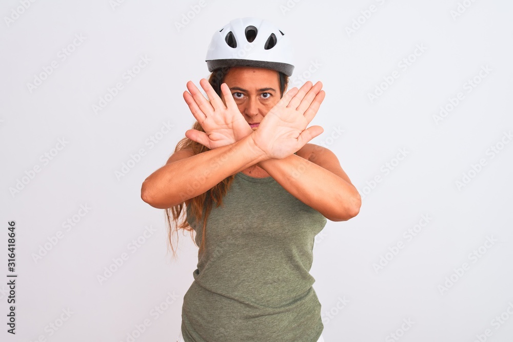 Middle age mature cyclist woman wearing safety helmet over isolated background Rejection expression crossing arms and palms doing negative sign, angry face Middle age mature cyclist woman wearing safety helmet over isolated background Rejection expression crossing arms and palms doing negative sign, angry face