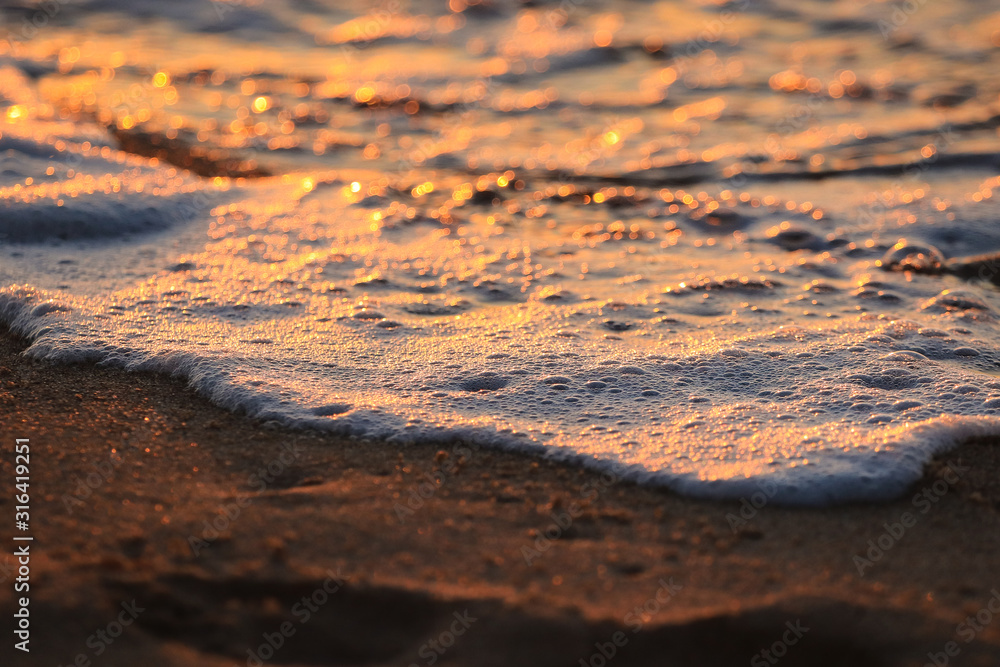 Wave with foam in a beach at the sunset
