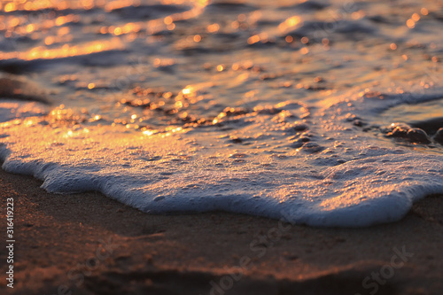 Wave with foam in a beach at the sunset