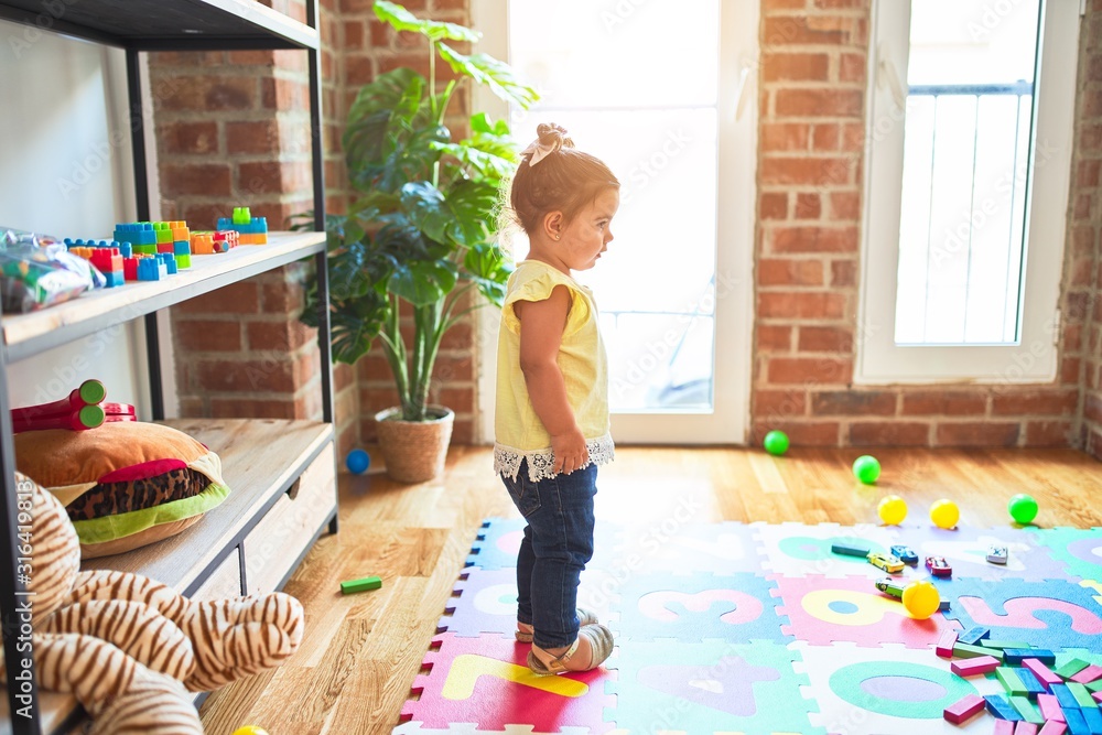 Beautiful toddler standing around lots of toys at kindergarten - obrazy, fototapety, plakaty 