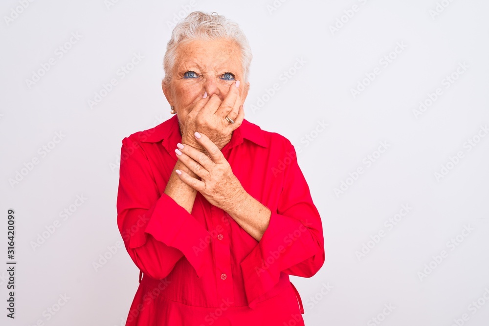 Senior grey-haired woman wearing red casual shirt standing over isolated white background smelling something stinky and disgusting, intolerable smell, holding breath with fingers on nose. Bad smells Senior grey-haired woman wearing red casual shirt standing over isolated white background smelling something stinky and disgusting, intolerable smell, holding breath with fingers on nose. Bad smells