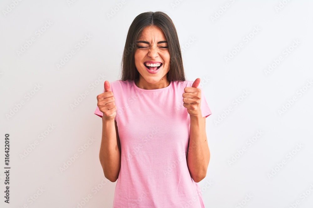Young beautiful woman wearing pink casual t-shirt standing over isolated white background excited for success with arms raised and eyes closed celebrating victory smiling. Winner concept. Young beautiful woman wearing pink casual t-shirt standing over isolated white background excited for success with arms raised and eyes closed celebrating victory smiling. Winner concept.