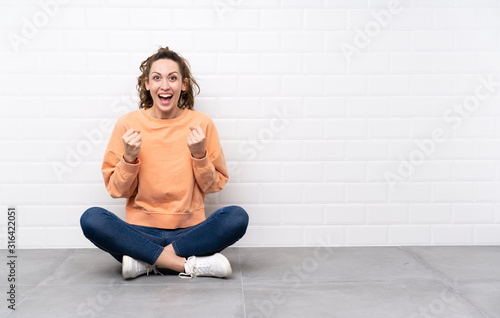 Young woman with curly hair sitting on the floor celebrating a victory