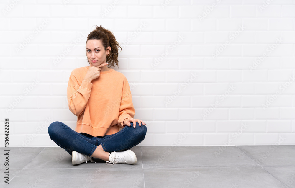 Young woman with curly hair sitting on the floor thinking an idea Young woman with curly hair sitting on the floor thinking an idea
