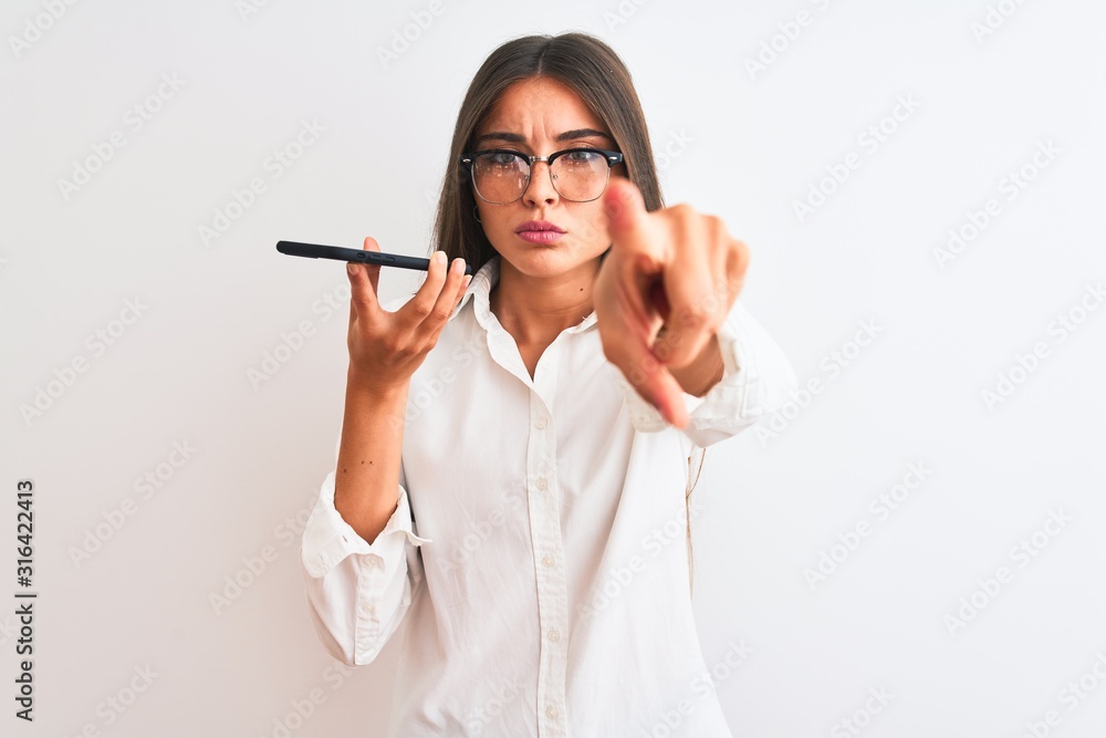 Woman wearing glasses sending message on smartphone over isolated white background pointing with finger to the camera and to you, hand sign, positive and confident gesture from the front Woman wearing glasses sending message on smartphone over isolated white background pointing with finger to the camera and to you, hand sign, positive and confident gesture from the front