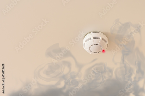 Smoke detector on the white ceiling for prevention fire with red emergency lamp and dark fume. Fire alarm for home, offices and hotels.