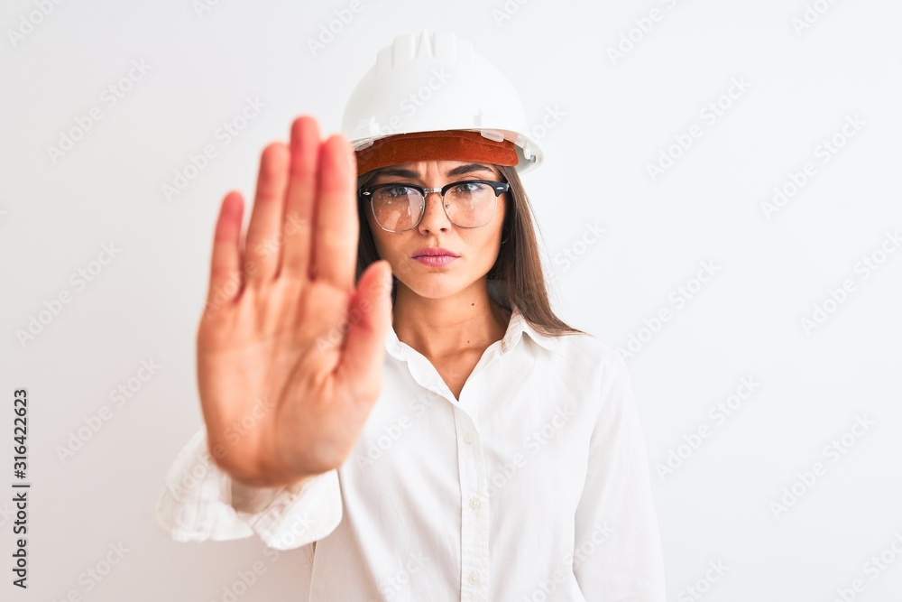 Young beautiful architect woman wearing helmet and glasses over isolated white background doing stop sing with palm of the hand. Warning expression with negative and serious gesture on the face. Young beautiful architect woman wearing helmet and glasses over isolated white background doing stop sing with palm of the hand. Warning expression with negative and serious gesture on the face.