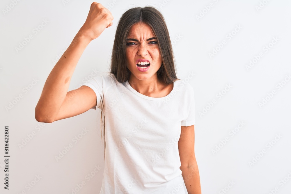 Young beautiful woman wearing casual t-shirt standing over isolated white background angry and mad raising fist frustrated and furious while shouting with anger. Rage and aggressive concept. Young beautiful woman wearing casual t-shirt standing over isolated white background angry and mad raising fist frustrated and furious while shouting with anger. Rage and aggressive concept.