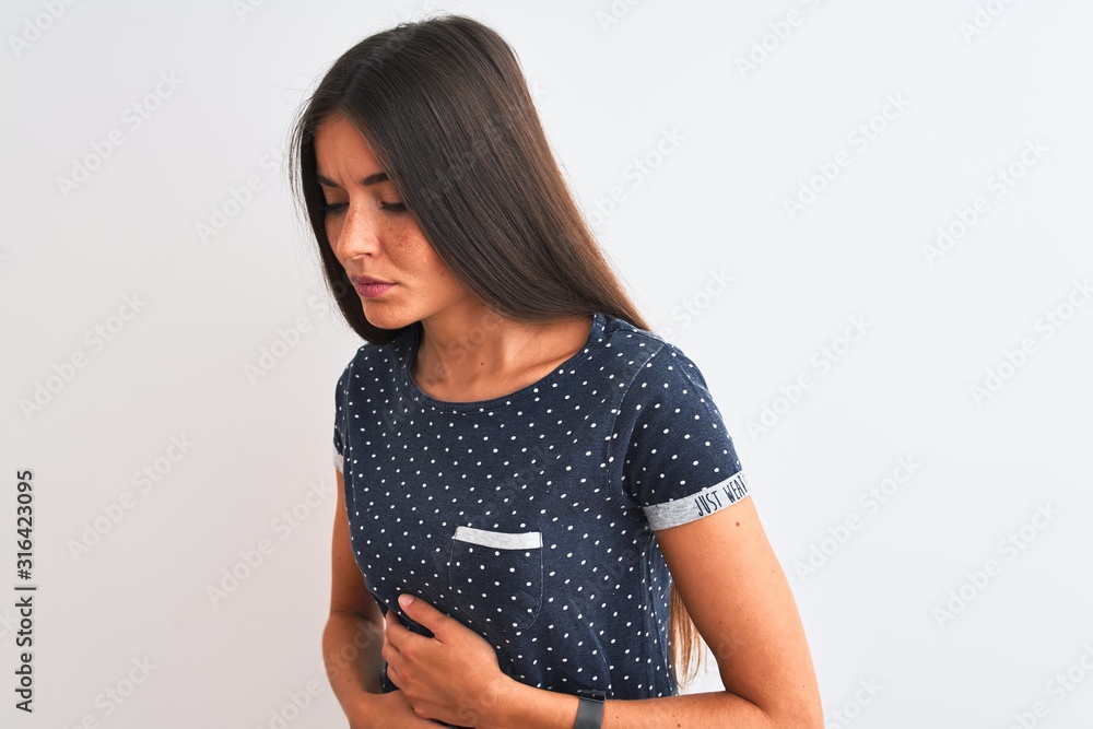 Young beautiful woman wearing blue casual t-shirt standing over isolated white background with hand on stomach because nausea, painful disease feeling unwell. Ache concept. Young beautiful woman wearing blue casual t-shirt standing over isolated white background with hand on stomach because nausea, painful disease feeling unwell. Ache concept.