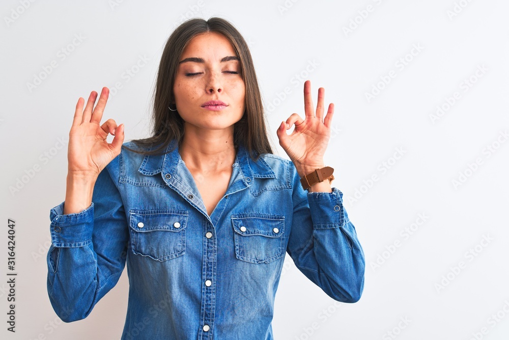 Young beautiful woman wearing casual denim shirt standing over isolated white background relax and smiling with eyes closed doing meditation gesture with fingers. Yoga concept. Young beautiful woman wearing casual denim shirt standing over isolated white background relax and smiling with eyes closed doing meditation gesture with fingers. Yoga concept.