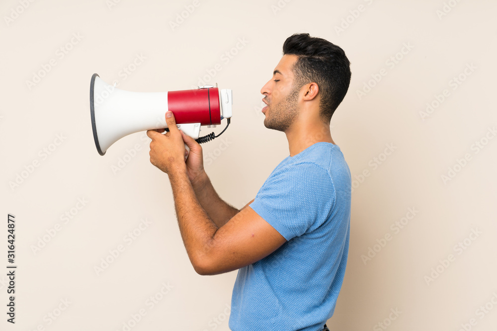Young handsome man over isolated background shouting through a megaphone Young handsome man over isolated background shouting through a megaphone