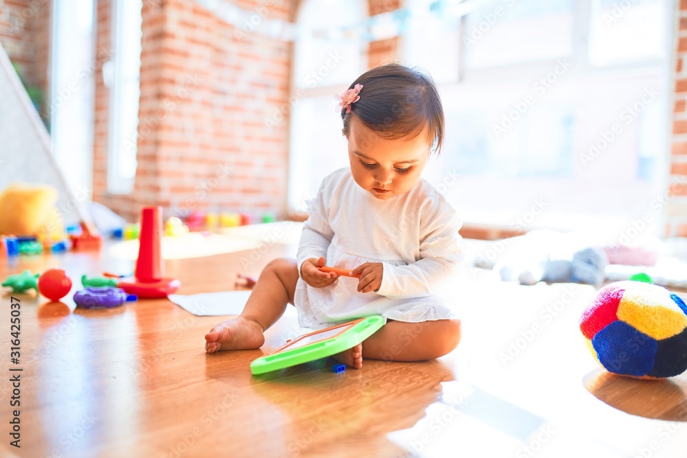 Beautiful infant happy at kindergarten around colorful toys drawing on magnetic blackboard