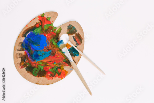 wooden art palette with blobs of paint and a brush on white background.