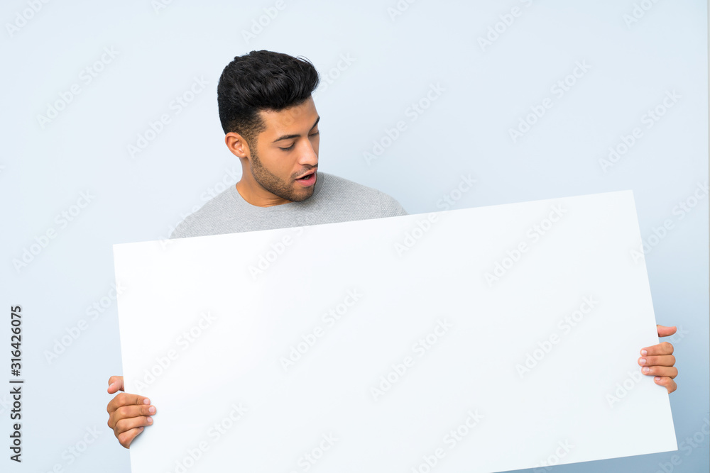 Young handsome man over isolated background holding an empty white placard for insert a concept Young handsome man over isolated background holding an empty white placard for insert a concept