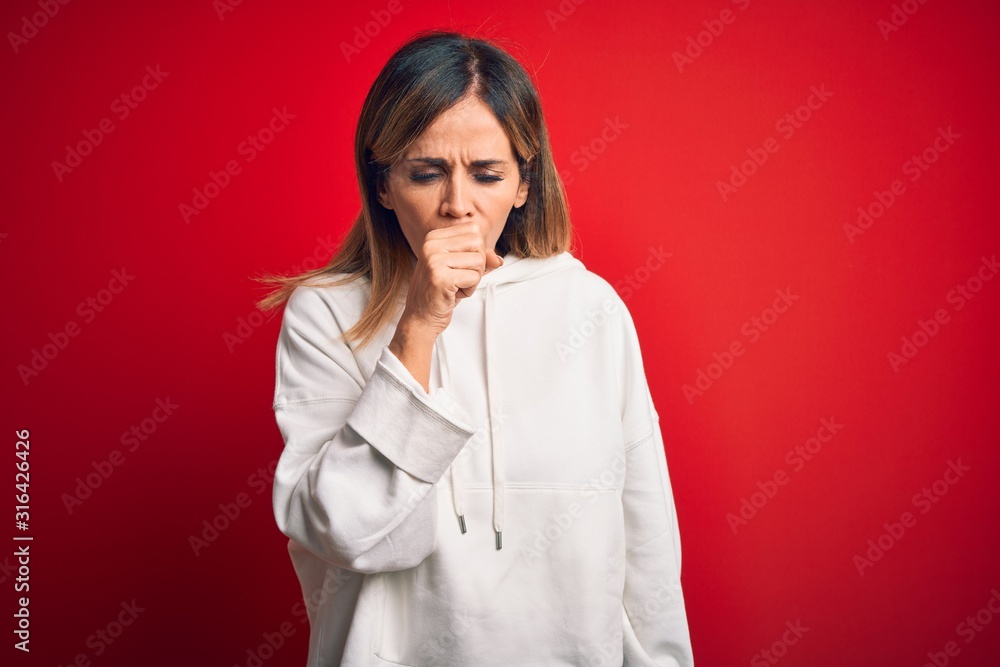 Middle age beautiful sportswoman wearing casual sweatshirt over isolated red background feeling unwell and coughing as symptom for cold or bronchitis. Health care concept.